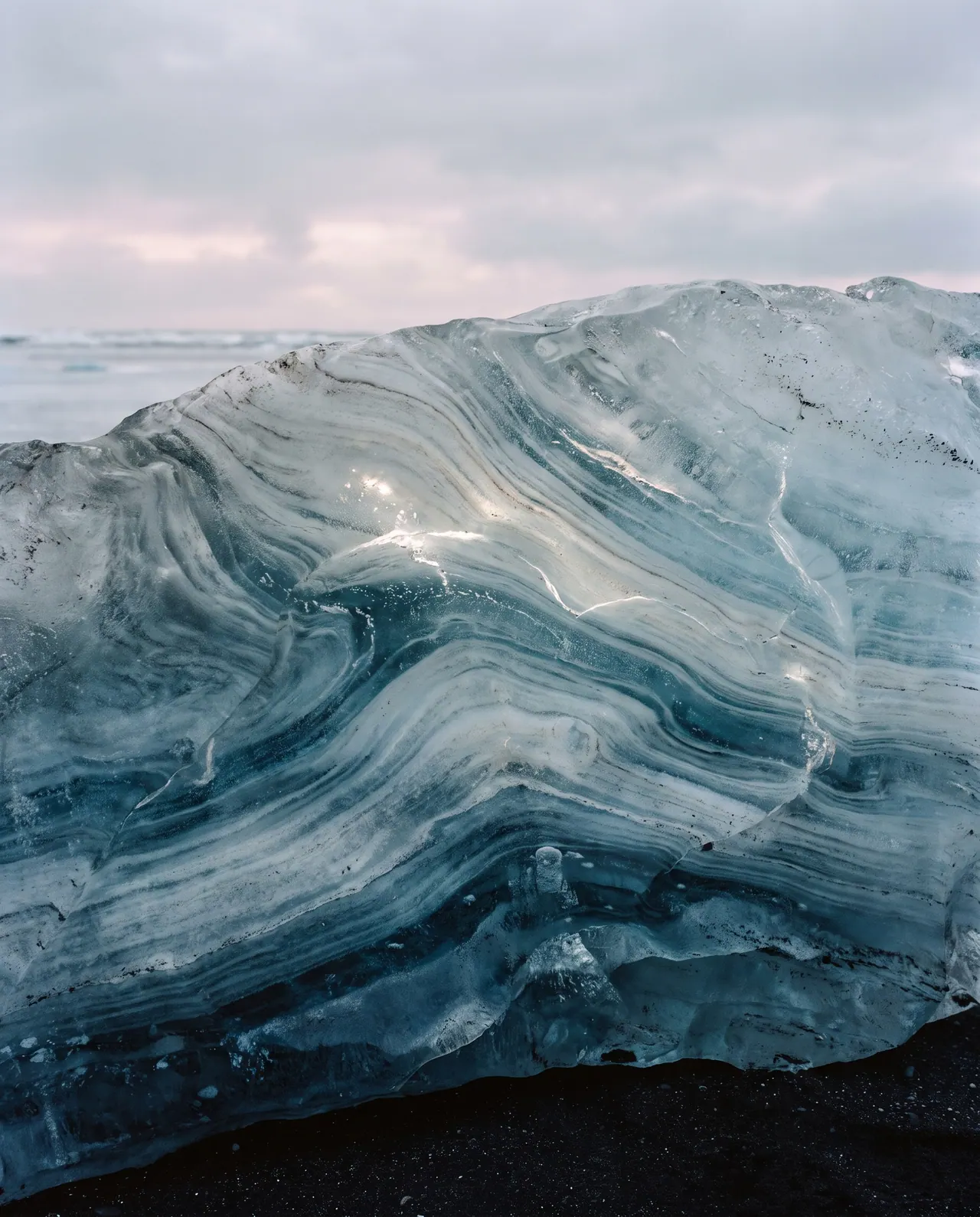 An abstract close view inside a block of glacial ice: layered bands of blue and white with curving lines that resemble the grain of wood.